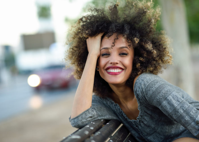 Young mixed woman with afro hairstyle smiling in urban background. Black girl wearing casual clothes.